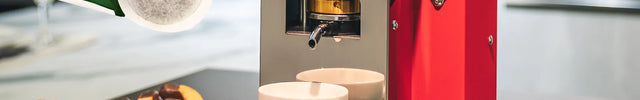 Machine à dosettes ESE Aroma Plus rouge sur un comptoir, avec une dosette et une tasse d'espresso